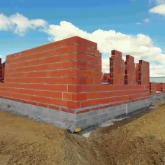 Budowa domu parterowego w toku. Widać fundamenty i wznoszone ściany z cegły.