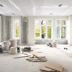 Salon w trakcie remontu, widoczne materiały budowlane, okna i drabina.