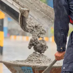 Robotnik w deszczu zasypuje taczkę betonem. Zastanawiasz się, ile kosztuje metr sześcienny betonu?