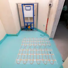 Instalacja ogrzewania podłogowego w łazience. Widać stelaż podtynkowy do WC, rury wodne i przygotowanie podłogi. To część cennika robót budowlanych.