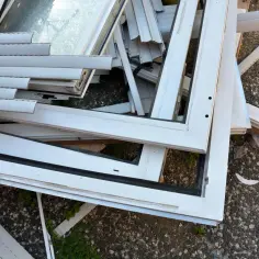 Stare okna PCV czekają na recykling. Widok pokazuje stos białych ram okiennych, niektóre z szybami, gotowe do przetworzenia.