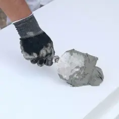Ręka w rękawicy nakłada zaprawę na styropian. Czas schnięcia kleju do styropianu zależy od warunków.