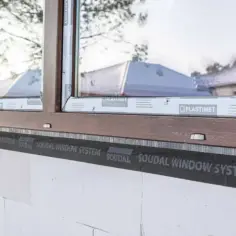 Ciepły montaż po zamontowaniu okien. Widoczna taśma Soudal Window System wokół drewnianej ramy okiennej w białej ścianie z bloczków.