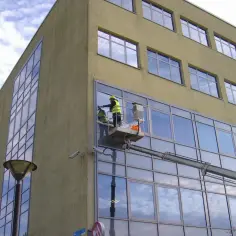 Pracownicy na podnośniku montują okno w nowoczesnym budynku.