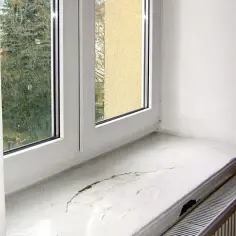 Uszkodzony parapet wewnętrzny przy oknie. Czy parapet wewnętrzny musi być wpuszczony w ścianę? Widać pęknięcia i odpryski.