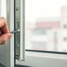 Dłoń dokręca śrubę w mechanizmie okna, przygotowując je do wymiany szyb w oknie plastikowym.