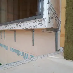 Montaż okien w domu szkieletowym. Metalowe wsporniki podtrzymują parapet, a ściana jest zabezpieczona membraną wiatroizolacyjną.