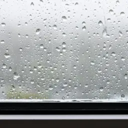 Krople deszczu na szybie, tworzące naturalny wzór. Jak wyciszyć parapet przed deszczem? Może warto po prostu cieszyć się widokiem?
