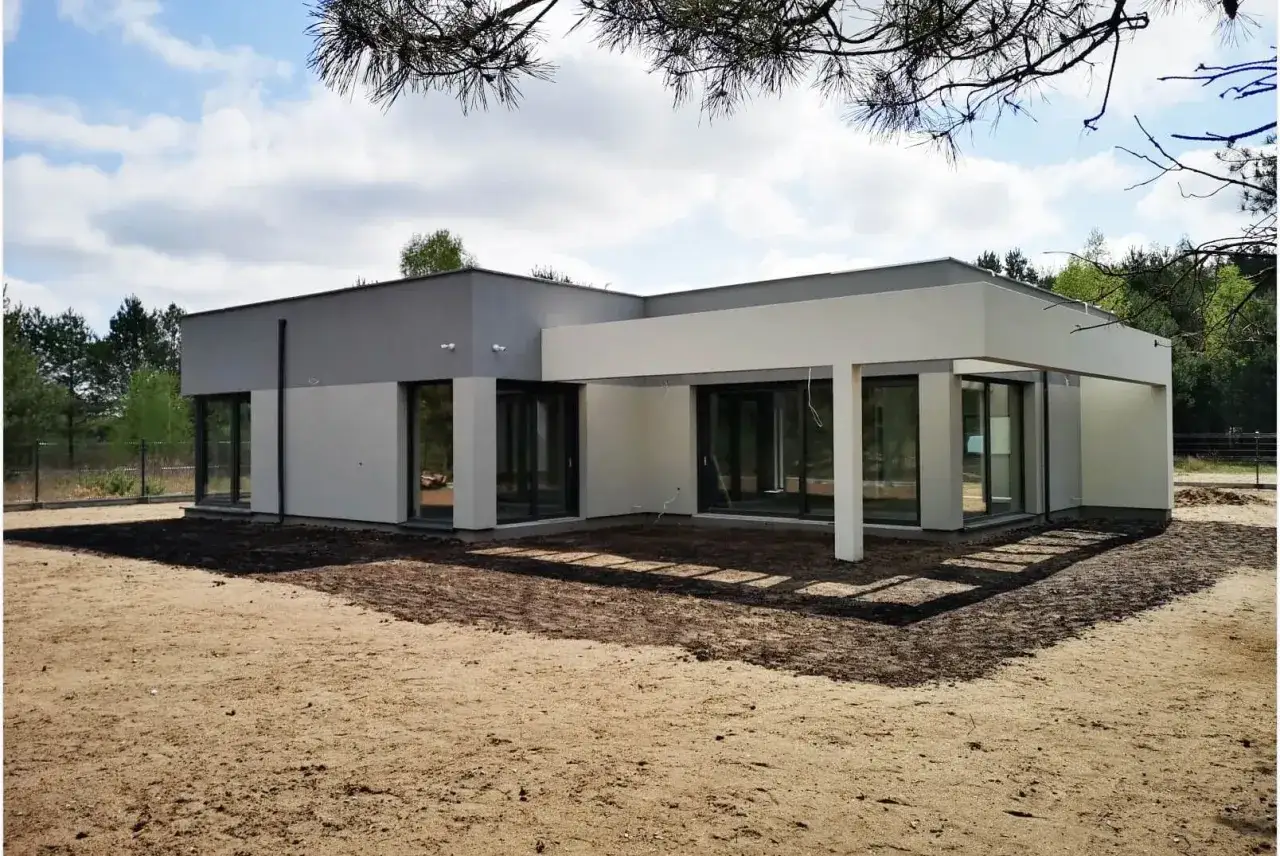 Nowoczesny dom parterowy w stanie surowym, otoczony piaskiem i zielenią. Zastanawiasz się, ile czasu trwa budowa domu parterowego?