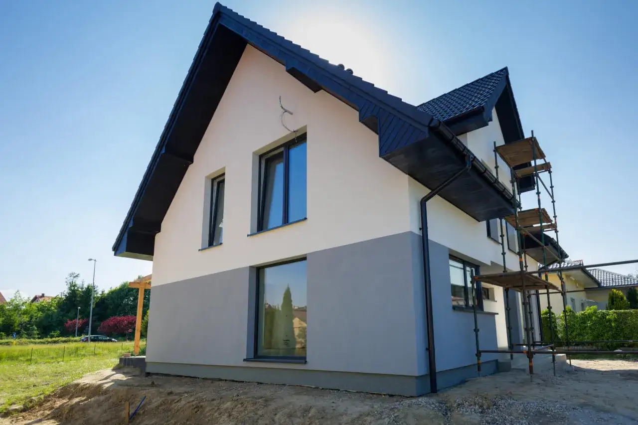 Nowy dom w trakcie budowy, z dwukolorową elewacją budynku i rusztowaniami.